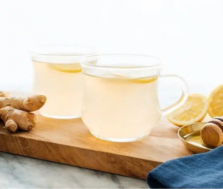 Homemade ginger tea in a cup with fresh ginger root and lemon slices
