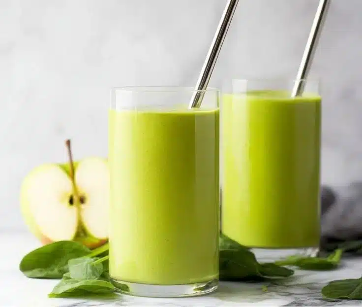 Spinach green apple smoothie in a glass with fresh ingredients nearby