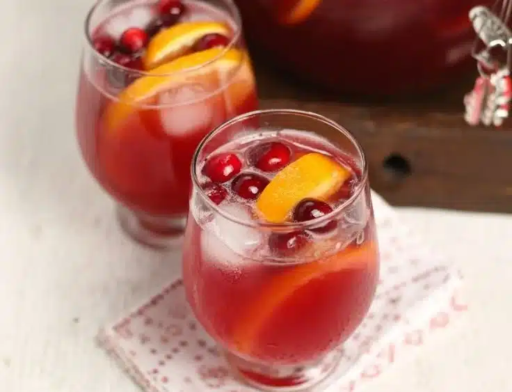 A festive glass of Holiday Punch garnished with fruits and herbs